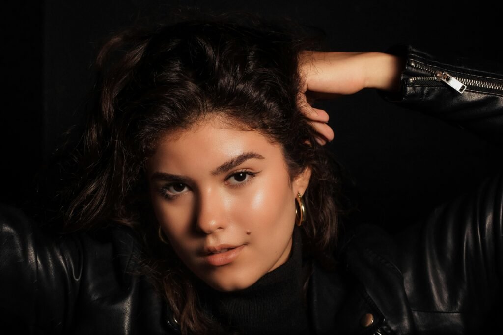 Close-up portrait of a woman in a black leather jacket against a black background, exuding confidence.