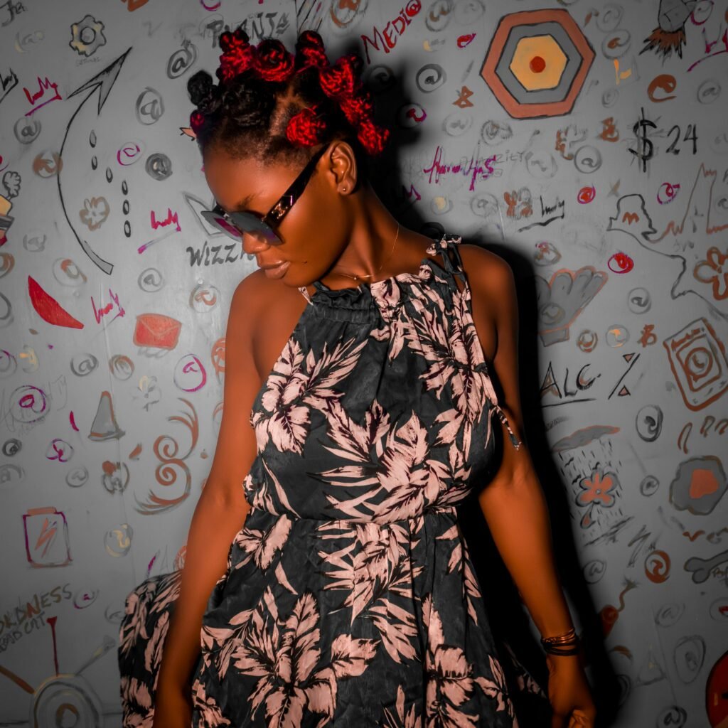 A fashionable woman in a floral dress and sunglasses poses against a graffiti-covered wall.